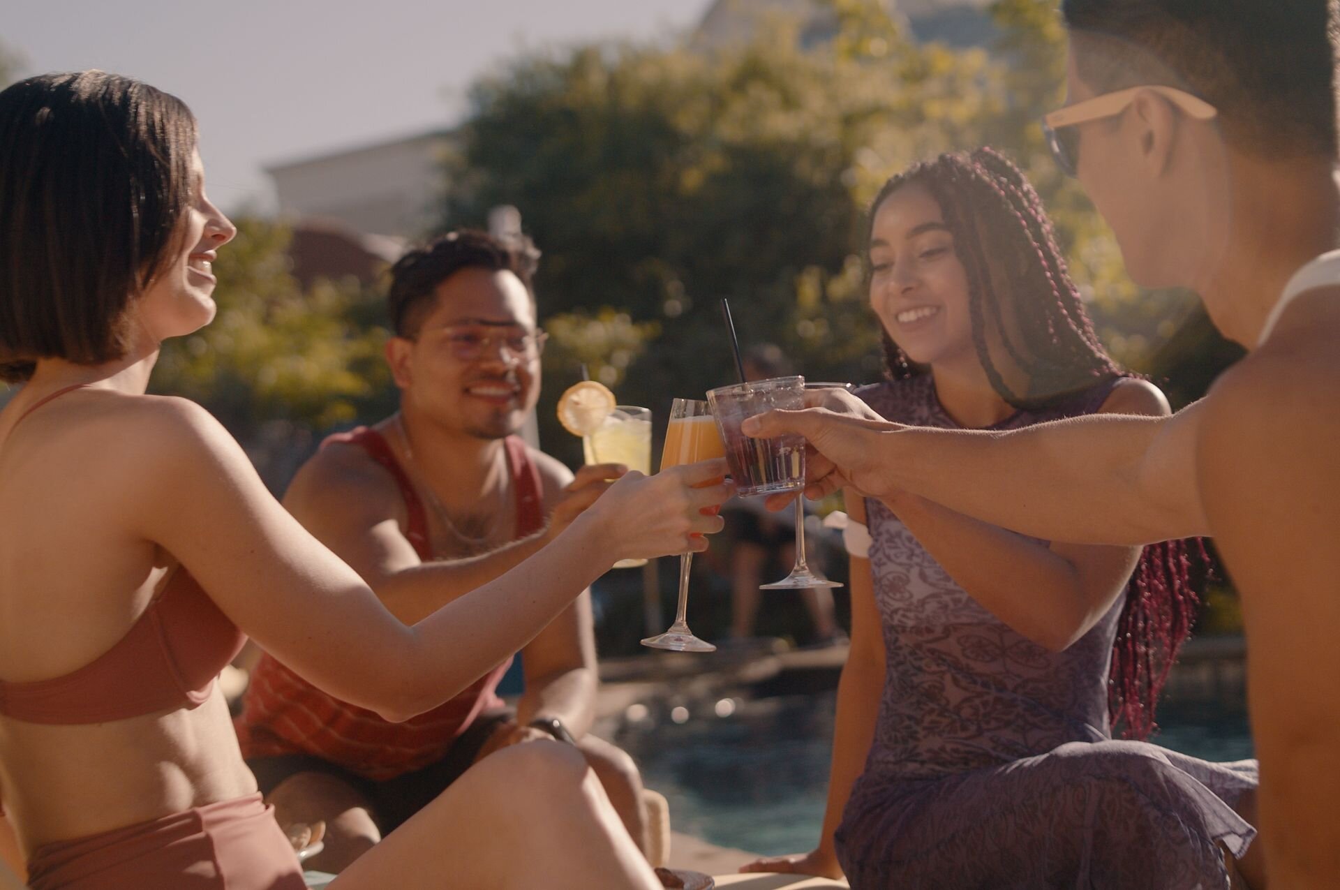 people holding up drinks by pool